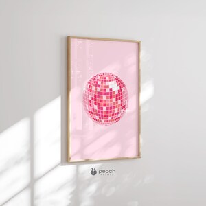 Op de afbeelding: Een roze discobal print met een witte achtergrond. De print is ingelijst in een licht houten lijst.