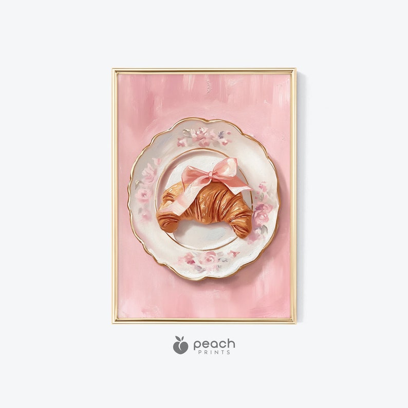 May include: A framed print featuring a croissant on a floral plate tied with a pink bow, set against a pink background. The plate has a gold trim and is decorated with pink roses. The print has a gold frame and the Peach Prints logo.