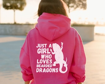 May include: A vibrant pink hoodie featuring the text "JUST A GIRL WHO LOVES BEARDED DRAGONS" and a white lizard graphic. The hoodie is paired with black shorts.