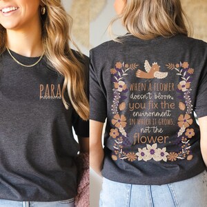 May include: A dark gray t-shirt with a floral design and the text "WHEN A FLOWER doesn't bloom you fix the environment IN WHICH IT GROWS, not the flower." on the back. The front of the shirt has the text "PARA profesional" in brown.