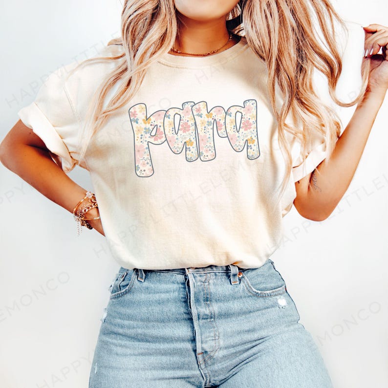 May include: Cream-colored t-shirt with the word "Mama" in a floral design. The letters are filled with pastel flowers in pink, yellow, and blue. The shirt is paired with blue jeans.