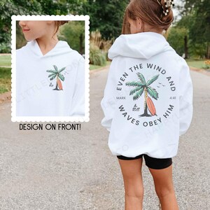 May include: White hoodie with a palm tree and surfboard graphic on the front and back. The back design includes the text "Even the Wind and Waves Obey Him" with a reference to Mark 4:41. The front design says "Be Still".