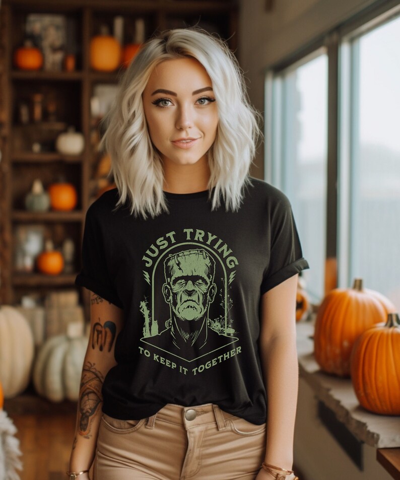 May include: Black t-shirt with a green graphic of Frankenstein's monster and the text "Just Trying To Keep It Together".