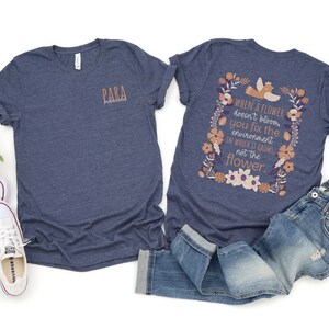 May include: Two navy blue t-shirts. The front of one t-shirt has the word "PARA" printed on it. The back of the other t-shirt has a floral design with the text "WHEN A FLOWER doesn't bloom you fix the environment IN WHICH IT GROWS, not the flower."