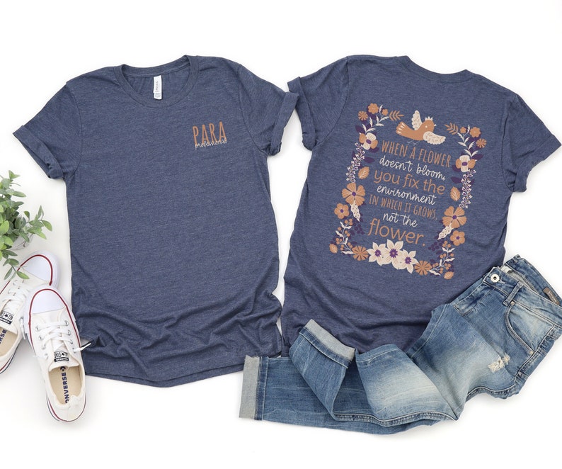 May include: Two navy blue t-shirts. The front of one t-shirt has the word "PARA" printed on it. The back of the other t-shirt has a floral design with the text "WHEN A FLOWER doesn't bloom you fix the environment IN WHICH IT GROWS, not the flower."