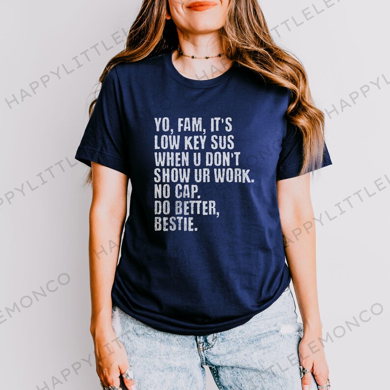 May include: Navy blue t-shirt with white text: "YO, FAM, IT'S LOW KEY SUS WHEN U DON'T SHOW UR WORK. NO CAP. DO BETTER, BESTIE." The shirt is a casual style.