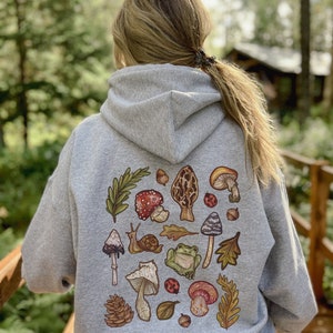 May include: A gray hooded sweatshirt with a colorful print of mushrooms, leaves, a snail, a frog, and ladybugs on the back.