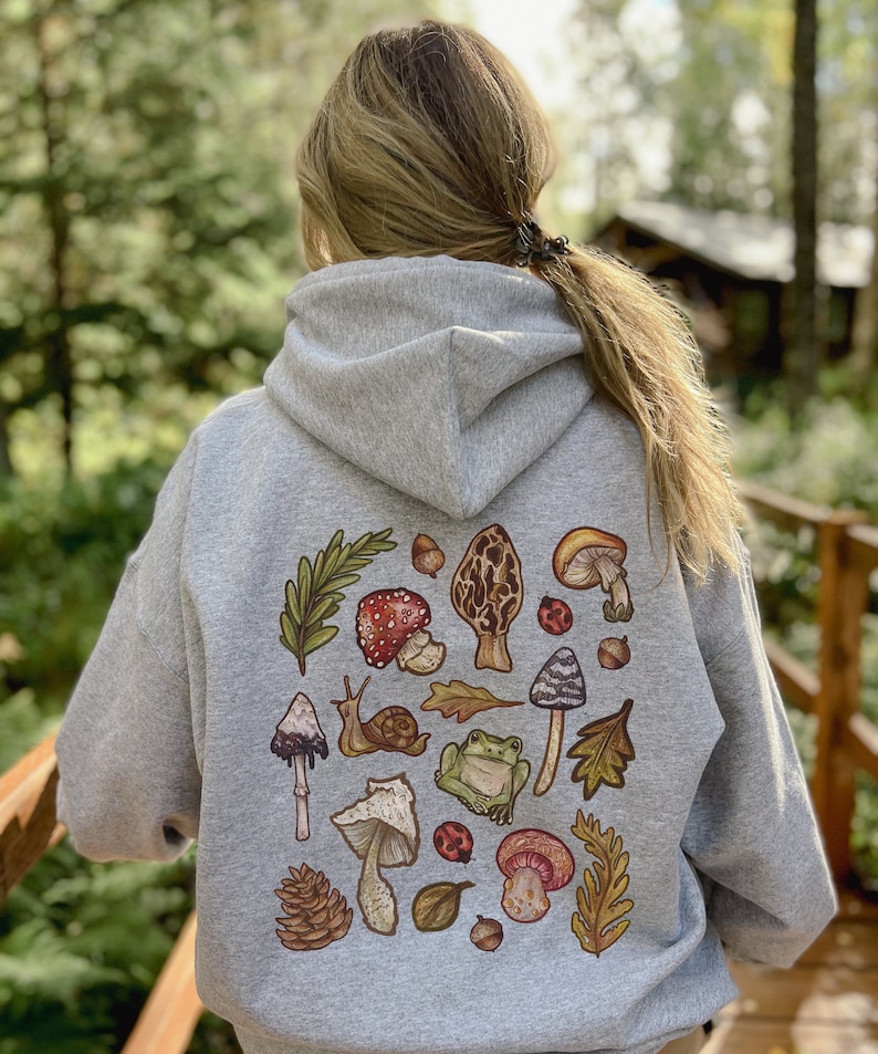 May include: A gray hooded sweatshirt with a colorful print of mushrooms, leaves, a snail, a frog, and ladybugs on the back.
