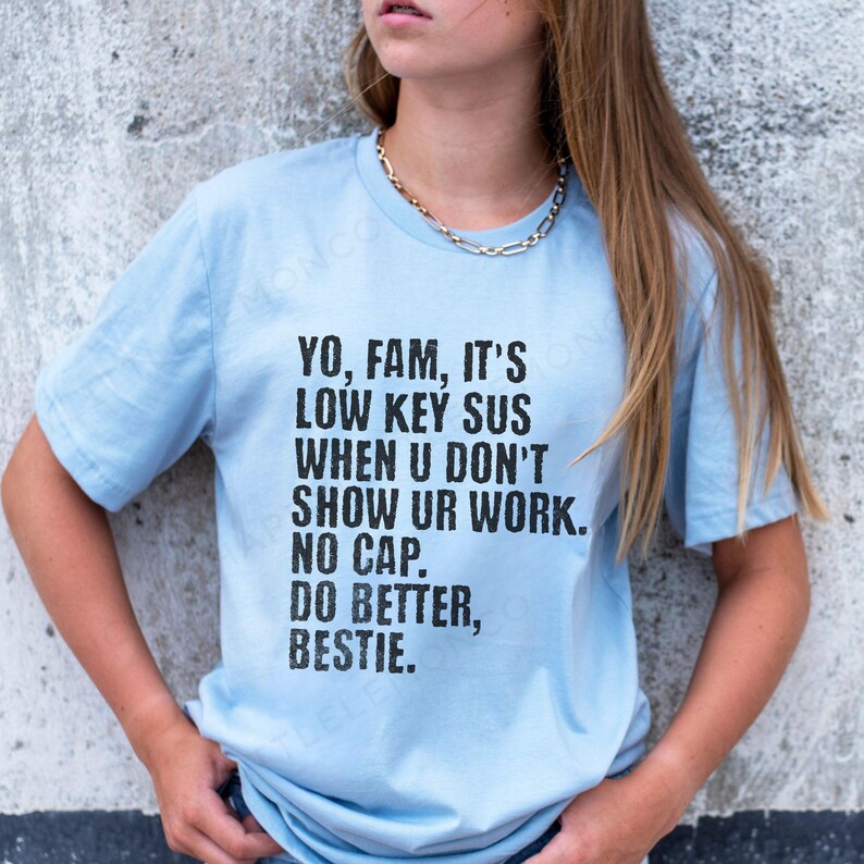 May include: Light blue t-shirt with black text. The text reads: "YO, FAM, IT'S LOW KEY SUS WHEN U DON'T SHOW UR WORK. NO CAP. DO BETTER, BESTIE."