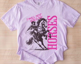May include: A lavender t-shirt with a graphic of a woman riding a horse. The text "I will not hold my horses" is printed in pink on the shirt.