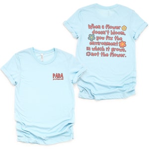 May include: Light blue t-shirt with a quote about flowers and the environment. The quote reads "When a flower doesn't bloom, you fix the environment in which it grows, not the flower." The text is surrounded by colorful flowers. The front of the shirt has the word "PARA" printed on it.