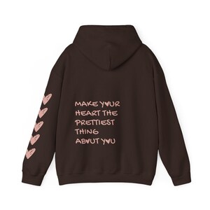 May include: A brown hoodie with a hood and long sleeves. The left sleeve has a series of pink hearts. The back of the hoodie has the text "MAKE YOUR HEART THE PRETTIEST THING ABOUT YOU" in pink.