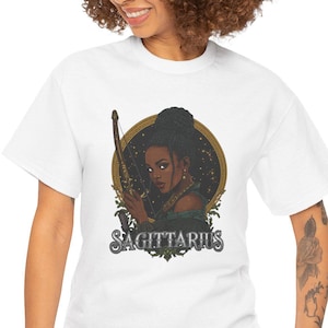 May include: White t-shirt featuring a detailed graphic of a woman with a bow and arrow, framed by a golden circle. The word "SAGITTARIUS" is printed below the image in a decorative font. The shirt is made of a soft, comfortable material.