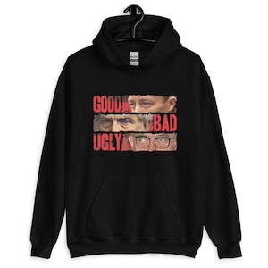 May include: Black hooded sweatshirt with a graphic design featuring the words "GOOD BAD UGLY" in red, with three sets of eyes. The sweatshirt has a front pocket and a drawstring hood.