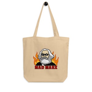 Puede incluir: Una bolsa de tela beige con una imagen de caricatura de Karl Marx con gafas de sol y barba, rodeado de llamas. El texto "MAD MARX" está impreso en rojo debajo de la imagen.