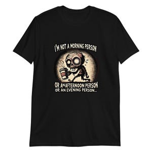 Könnte beinhalten: Schwarzes T-Shirt mit einer Cartoon-Illustration eines Zombies, der eine Tasse Kaffee hält. Der Text "Ich bin kein Morgenmensch, kein Nachmittagmensch und kein Abendmensch..." ist auf dem T-Shirt aufgedruckt.