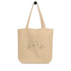 May include: A beige canvas tote bag with a black line drawing of musical notes on the front.