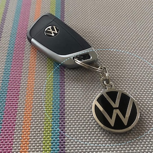 May include: A silver car key with a black Volkswagen logo on the key fob. The key fob has a black and silver Volkswagen logo on it.