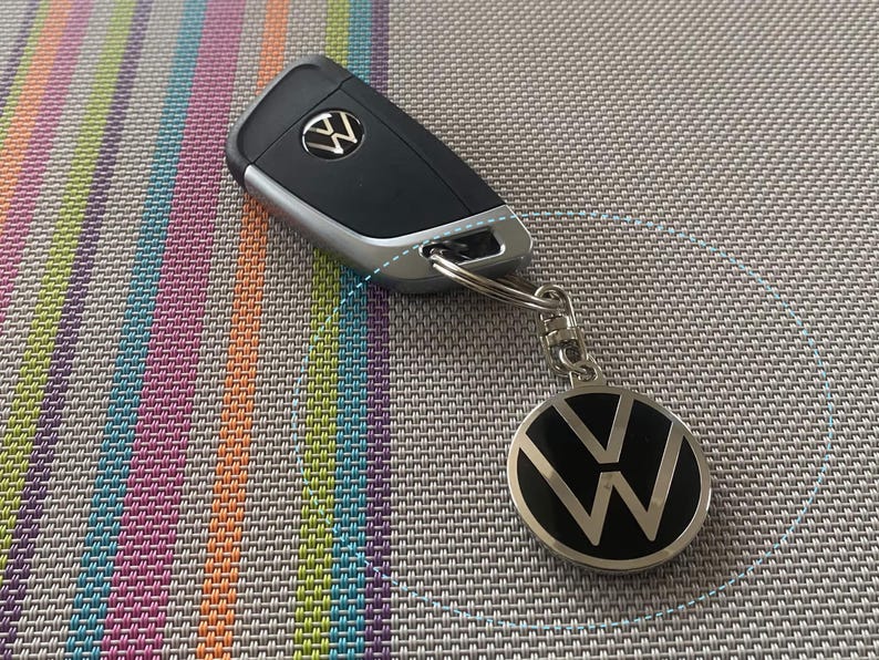May include: A silver car key with a black Volkswagen logo on the key fob. The key fob has a black and silver Volkswagen logo on it.