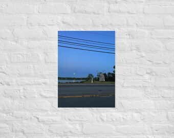 May include: A blue sky with a few clouds and power lines. A small windmill is in the distance, with a body of water behind it. The scene is lit by a bright yellow moon.