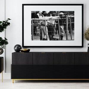 May include: Black and white framed photograph depicting gauchos leaning on a fence, observing horses. The photograph is displayed above a black wooden cabinet with gold accents, a bonsai tree, and decorative items.