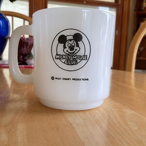 Puede incluir: Taza de cer&aacute;mica blanca con el logotipo de Mickey Mouse Club en negro. La taza tiene un asa redondeada y una base apilada. El texto "Walt Disney Productions" est&aacute; impreso debajo del logotipo. Un objeto de colecci&oacute;n vintage.