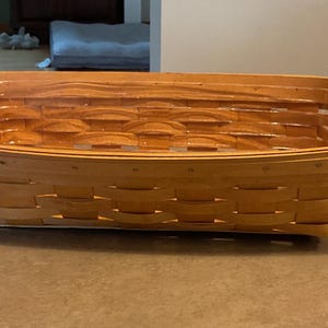 May include: A rectangular woven basket made of light brown wood strips with a smooth finish. The basket features a classic over-under weave pattern with a reinforced rim and a flat base, providing a structured and open storage container design.