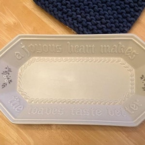 May include: A light gray rectangular serving platter with the words "a joyous heart makes the loaves taste better" embossed on the surface. The platter has a floral design and a rope-like border.