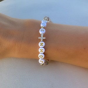 May include: White beaded bracelet with gold letters spelling "JOHN" and a small cross charm with clear rhinestones.