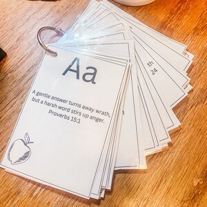 May include: A set of white cards with black lettering and a black and white illustration of an apple. The cards are labeled with the letter "A" and the phrase "A gentle answer turns away wrath, but a harsh word stirs up anger. Proverbs 15:1".