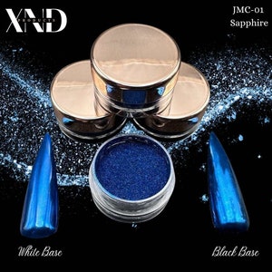 May include: A small jar of blue glitter with the text "JMC-01 Sapphire" on a white background. The glitter is shown on a white and black nail polish base.