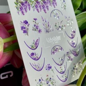 Pode incluir: Uma folha de autocolantes de transferência de água para unhas com desenhos florais roxos, incluindo glicínias e lavanda. A folha inclui vários arranjos florais e desenhos de semicírculos. O texto "UAslider water stickers - CF 462" é visível.