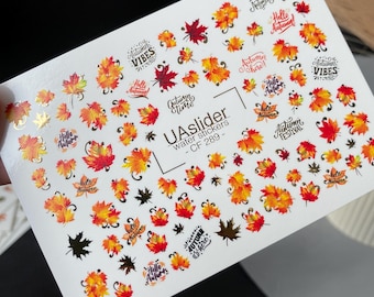 Puede incluir: Hoja de pegatinas de agua para uñas con diseños otoñales. Las pegatinas presentan hojas rojas, naranjas y amarillas, junto con frases como "Hello Autumn" y "Autumn Vibes". El producto está etiquetado como "UAslider water stickers - CF 289".
