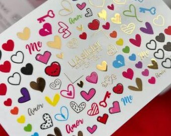 May include: Nail art sticker sheet with diverse heart designs in red, pink, gold, black, and other colours. Some hearts have key and lock designs, and the words "me" and "amor" are also included.