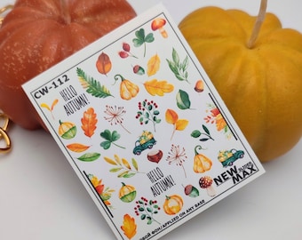 Puede incluir: Una hoja de pegatinas para uñas con temática otoñal. Las pegatinas muestran calabazas, hojas, bellotas y un camión que lleva calabazas. El texto "Hello Autumn!" aparece dos veces en la hoja. La hoja está etiquetada como "CW-112" y "New Slider Max".