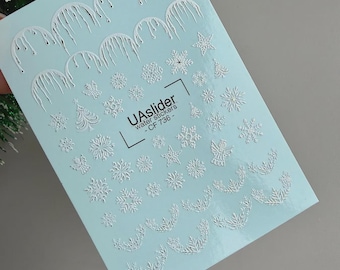 Puede incluir: Una hoja azul claro de pegatinas al agua con diseños blancos en relieve que incluyen carámbanos, varios patrones de copos de nieve, árboles de Navidad y ángeles. El texto central dice UAslider water stickers - CF 736 - con un diseño de corchetes.