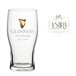May include: A clear pint glass with the Guinness logo and text. The logo features a gold harp. The text on the glass reads "GUINNESS" above "Any Message" and "Any Font". A logo for "ASTIRA PERSONALIZED GIFTS" is to the right.