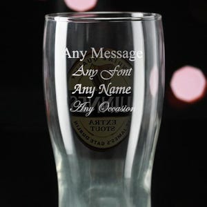 May include: A clear pint glass with the words "Any Message, Any Font, Any Name, Any Occasion" in white script. The glass has a logo in the center. The background is dark with soft pink orbs.