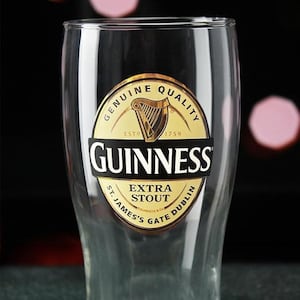 May include: A clear pint glass with the Guinness logo. The logo is a gold and black emblem with the word "Guinness" in bold letters, and the words "Extra Stout" and "St. James's Gate Dublin" are also visible.