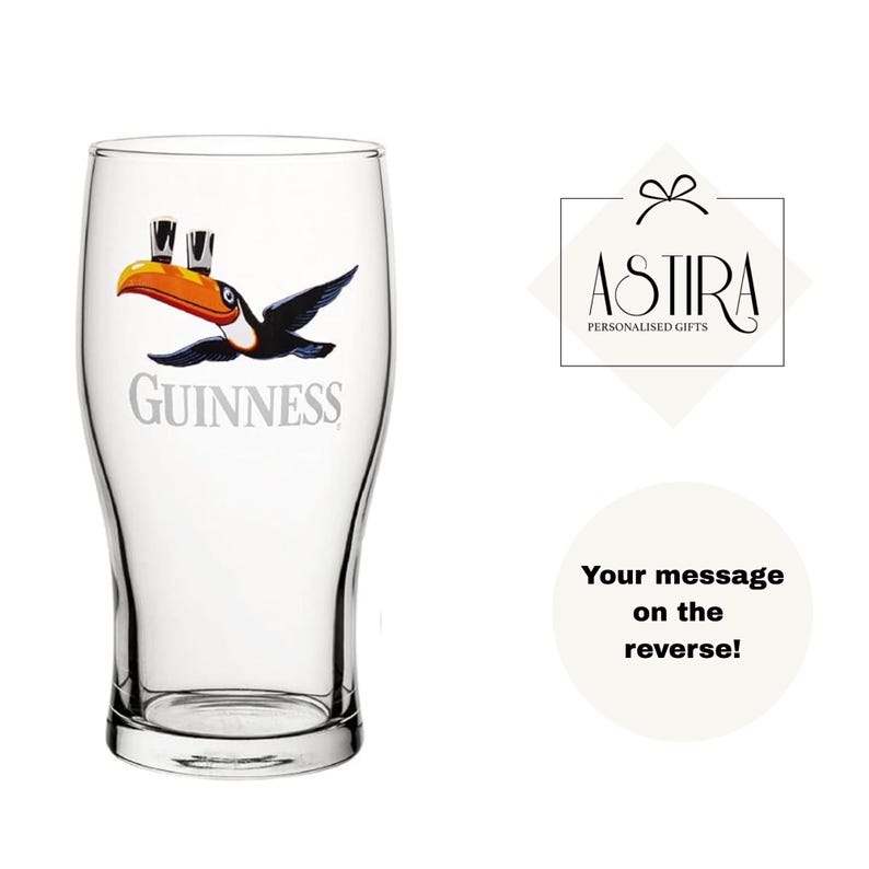 May include: A clear pint glass featuring the Guinness logo and a toucan design. The toucan has a yellow beak and is holding two small glasses of beer. The glass has a curved shape and a thick base.