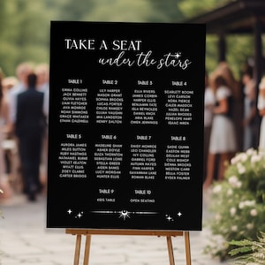 May include: A black wedding seating chart on a wooden easel. The chart features white text with guest names organized by table number. The title "Take a Seat under the Stars" is at the top, with decorative star accents.