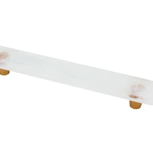 Puede incluir: Tirador de armario de vidrio blanco con pomos de metal dorado. El tirador es rectangular y tiene un borde ligeramente redondeado.