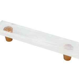 Peut inclure: Une poignée de tiroir rectangulaire transparente avec deux boutons en métal doré. La poignée a un effet marbré subtil.