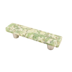 Puede incluir: Un tirador rectangular para armario con un patrón moteado verde y blanco. El tirador tiene un acabado pulido y está montado sobre dos postes cilíndricos plateados. Este herraje es adecuado para cajones y armarios.
