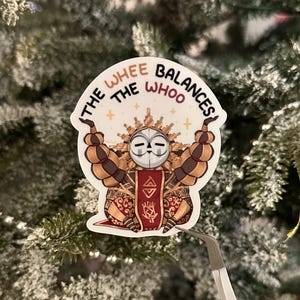 Könnte beinhalten: Ein Aufkleber mit einem stilisierten Charakter mit weißer Maske, braunen und beigefarbenen, segmentierten Armen und einem rot-goldenen Banner. Der Text "THE WHEE BALANCES THE WHOO" ist oben auf dem Aufkleber angeordnet.