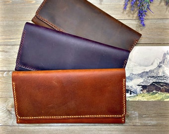 May include: Three leather wallets in different colors: brown, purple, and orange. The wallets are laid out on a wooden surface with a sprig of lavender flowers.