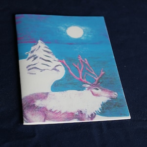 Può includere: Un biglietto dipinto a mano con una renna con corna rosa in piedi in un paesaggio innevato sotto una luna piena. Lo sfondo è un cielo blu con nuvole rosa.