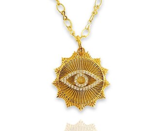 May include: Gold necklace with a pendant featuring a diamond-encrusted evil eye design. The pendant is surrounded by a sunburst pattern.
