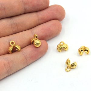 May include: Five gold-tone metal clasps with a textured surface. The clasps have a loop at the top for attaching to a chain or cord.