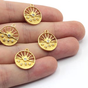 May include: Four gold-toned metal charms with a sun and stars design. Each charm features a sun with a clear rhinestone in the center and five smaller rhinestones around the sun.